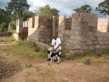 Fr. Combey sits beside the half-built structure of the Holy Rosary Blama Preschool.